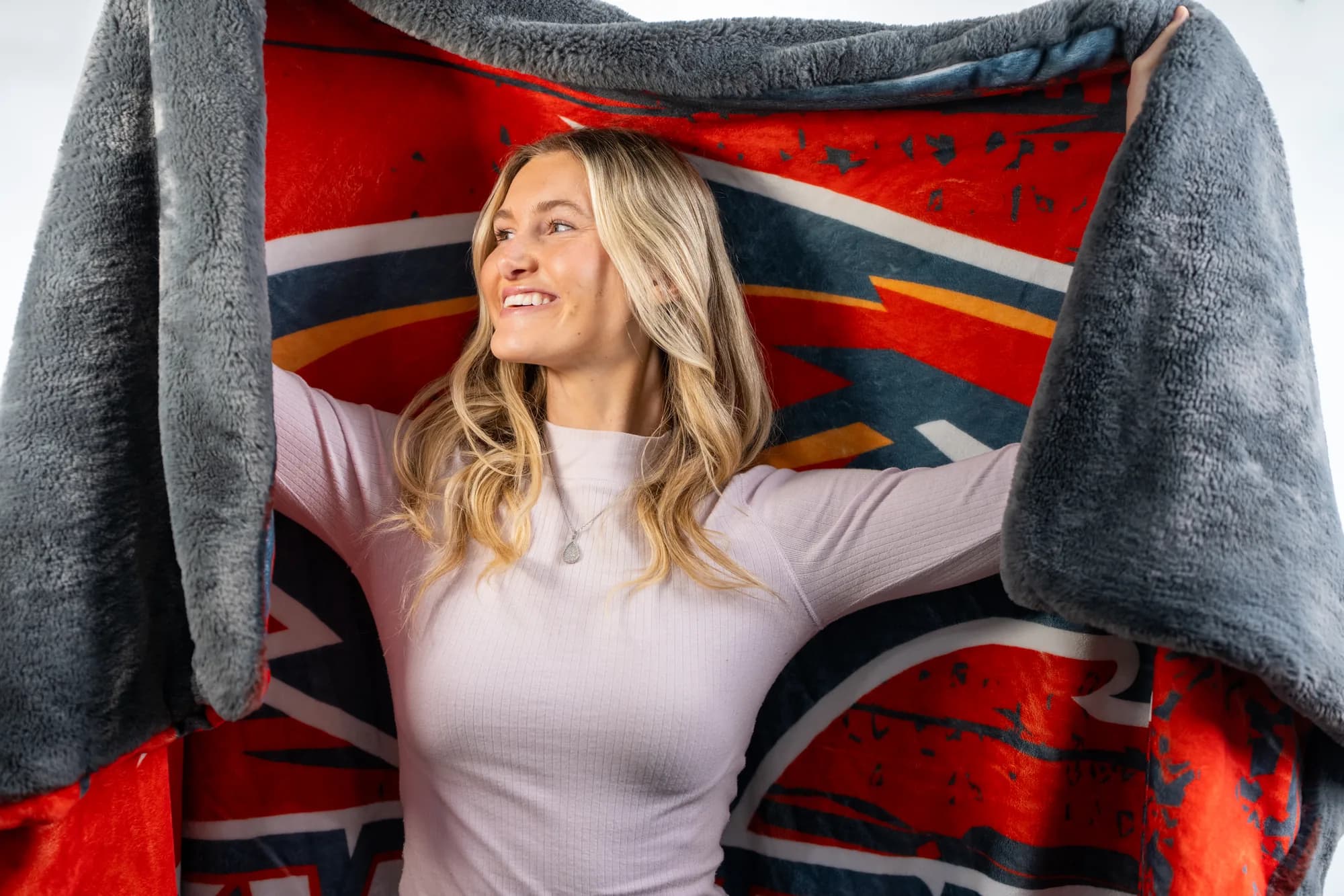 A customer holding open a Swanky mascot blanket, gray faux-fur back and full-color print front